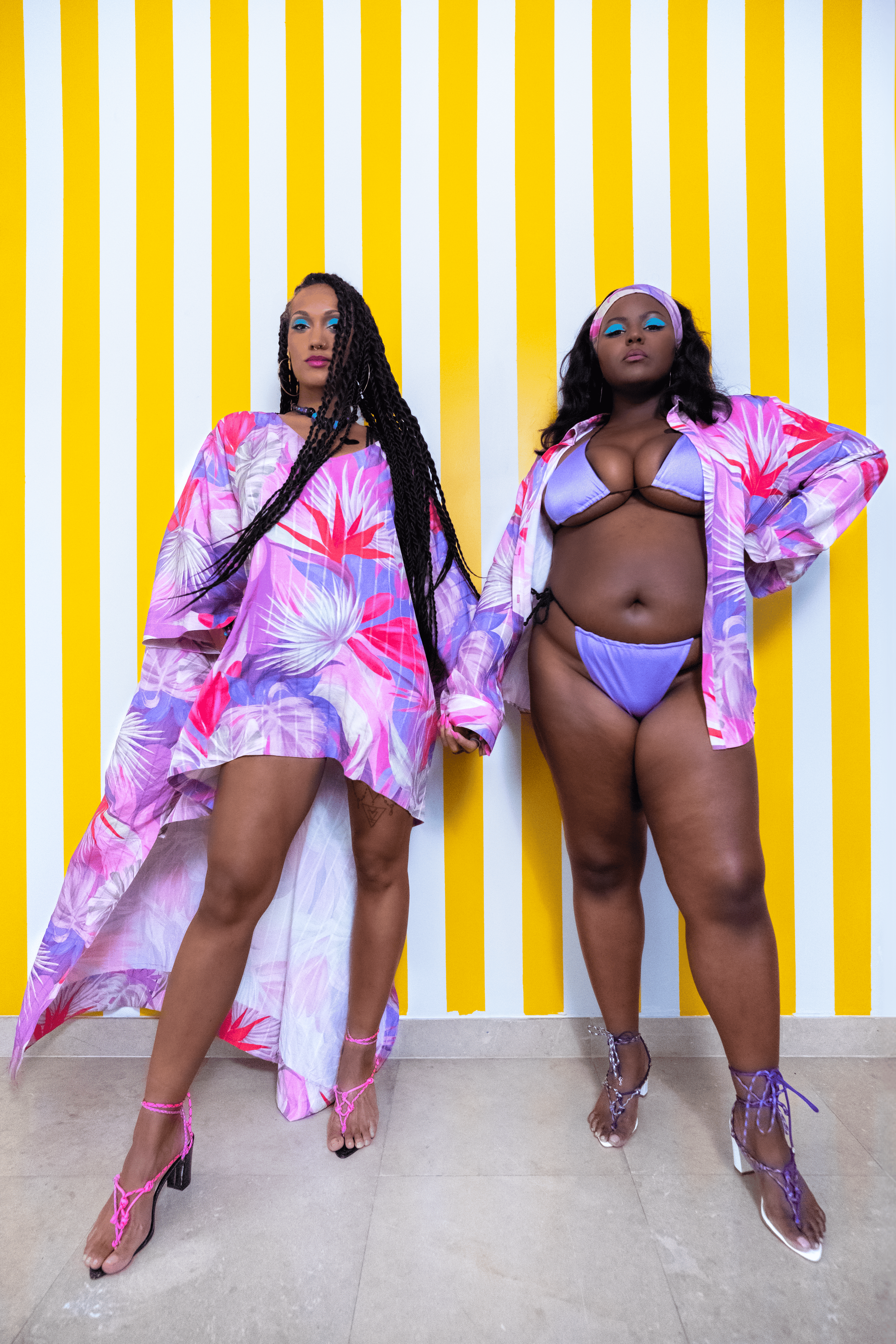 Two women in colorful outfits against a yellow and white striped background