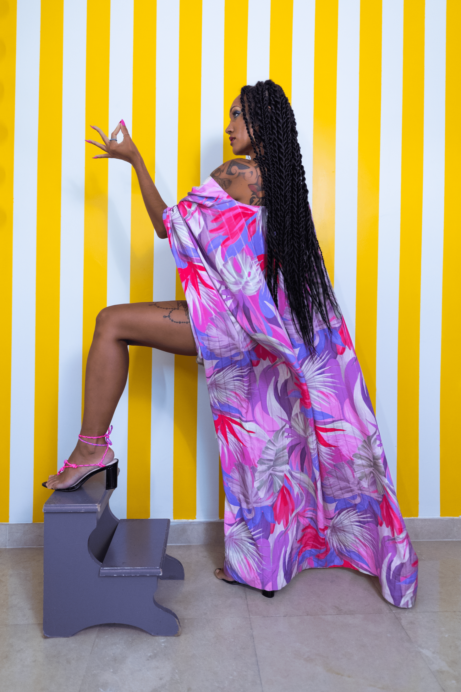 Woman in a colorful dress posing against a yellow and white striped wall.