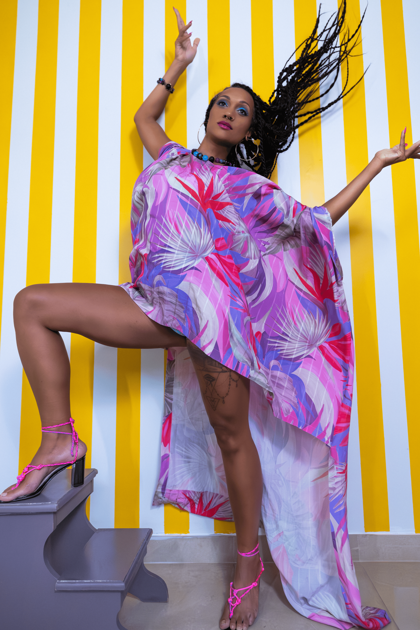 Woman in a colorful dress posing against a yellow and white striped wall.