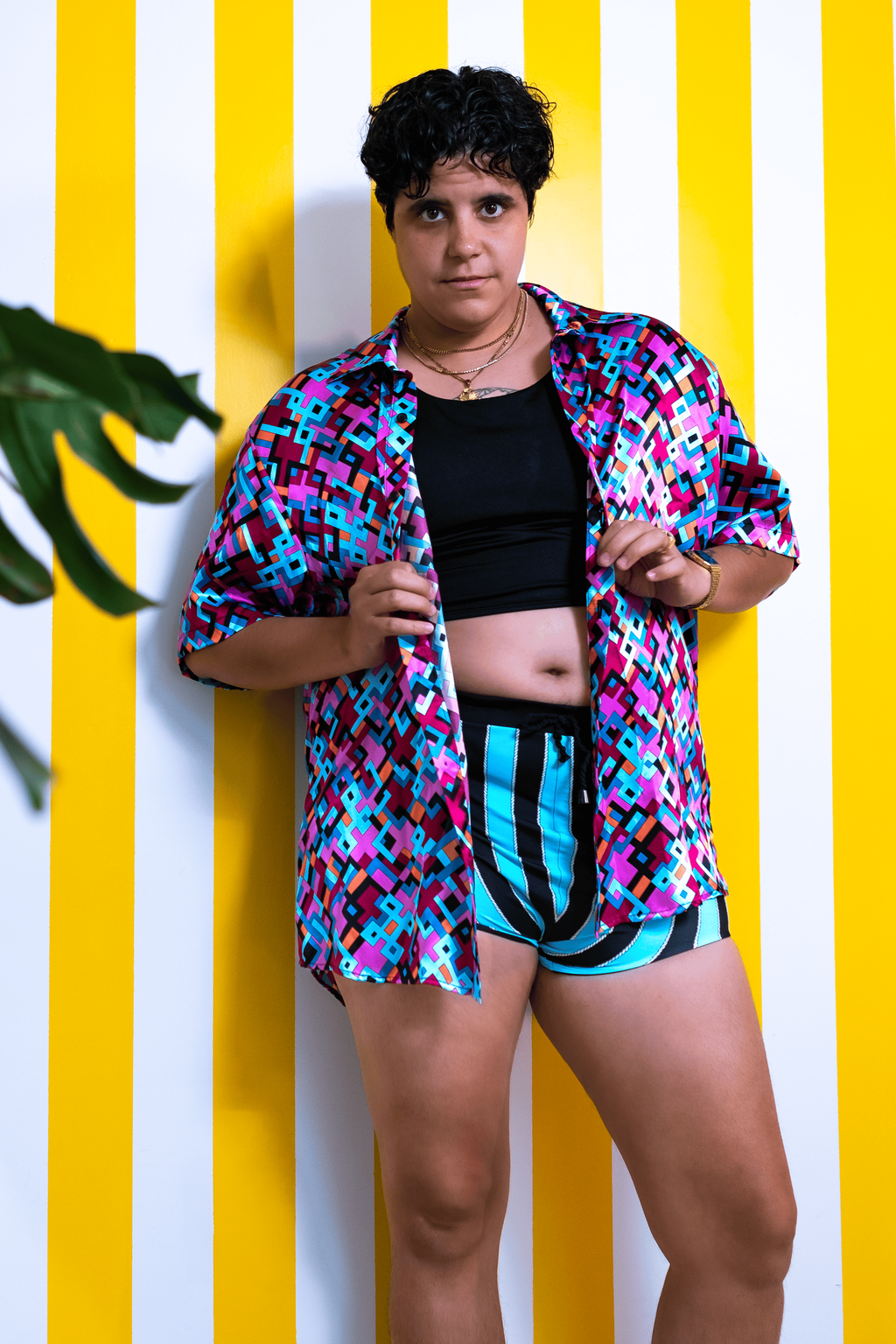 Person wearing a colorful shirt and black shorts against a yellow and white striped wall.