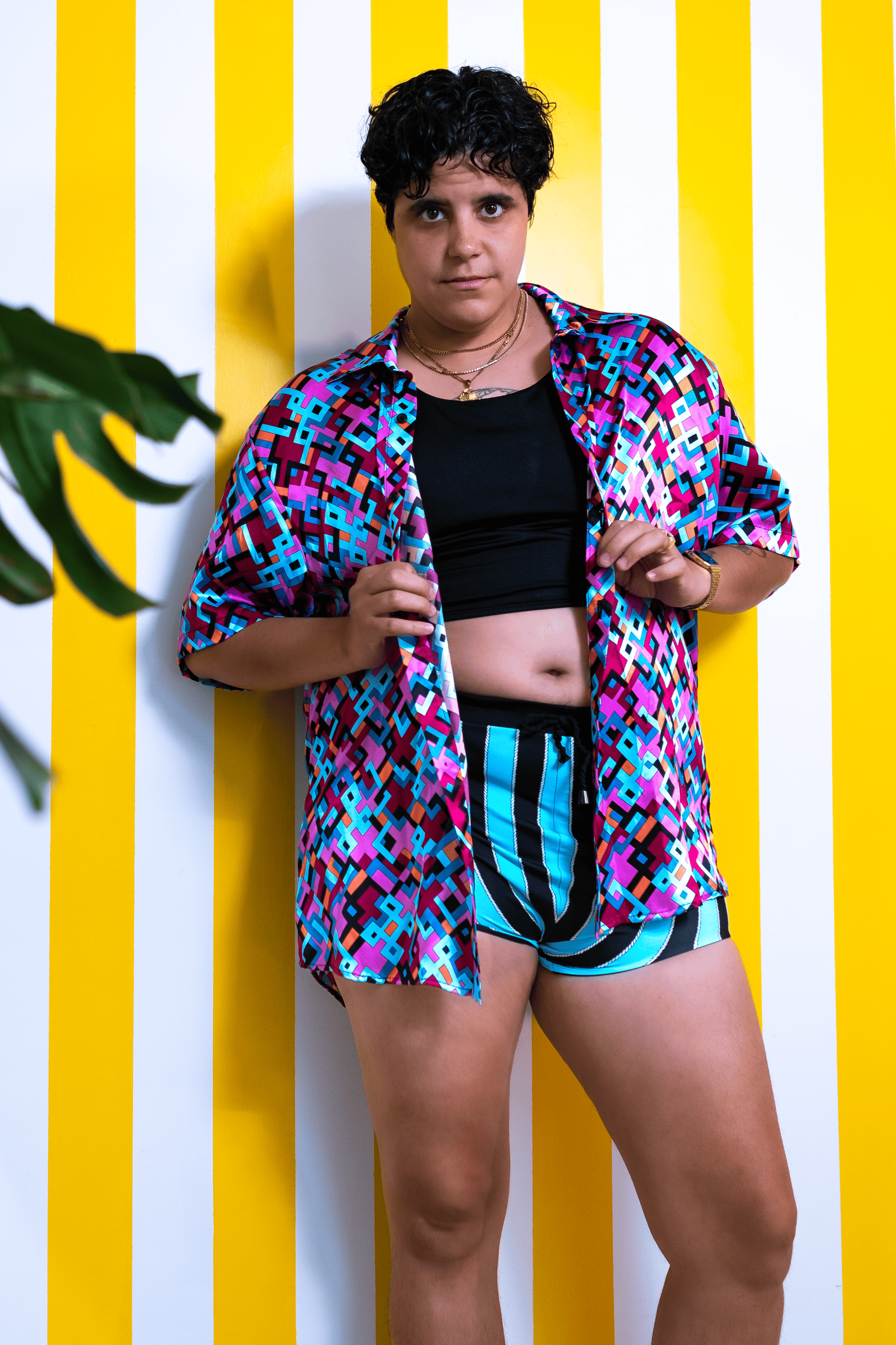 Person wearing a colorful shirt and black shorts against a yellow and white striped wall.