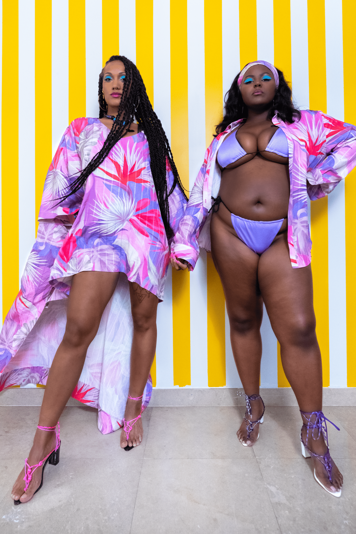 Two women in colorful outfits against a yellow and white striped background