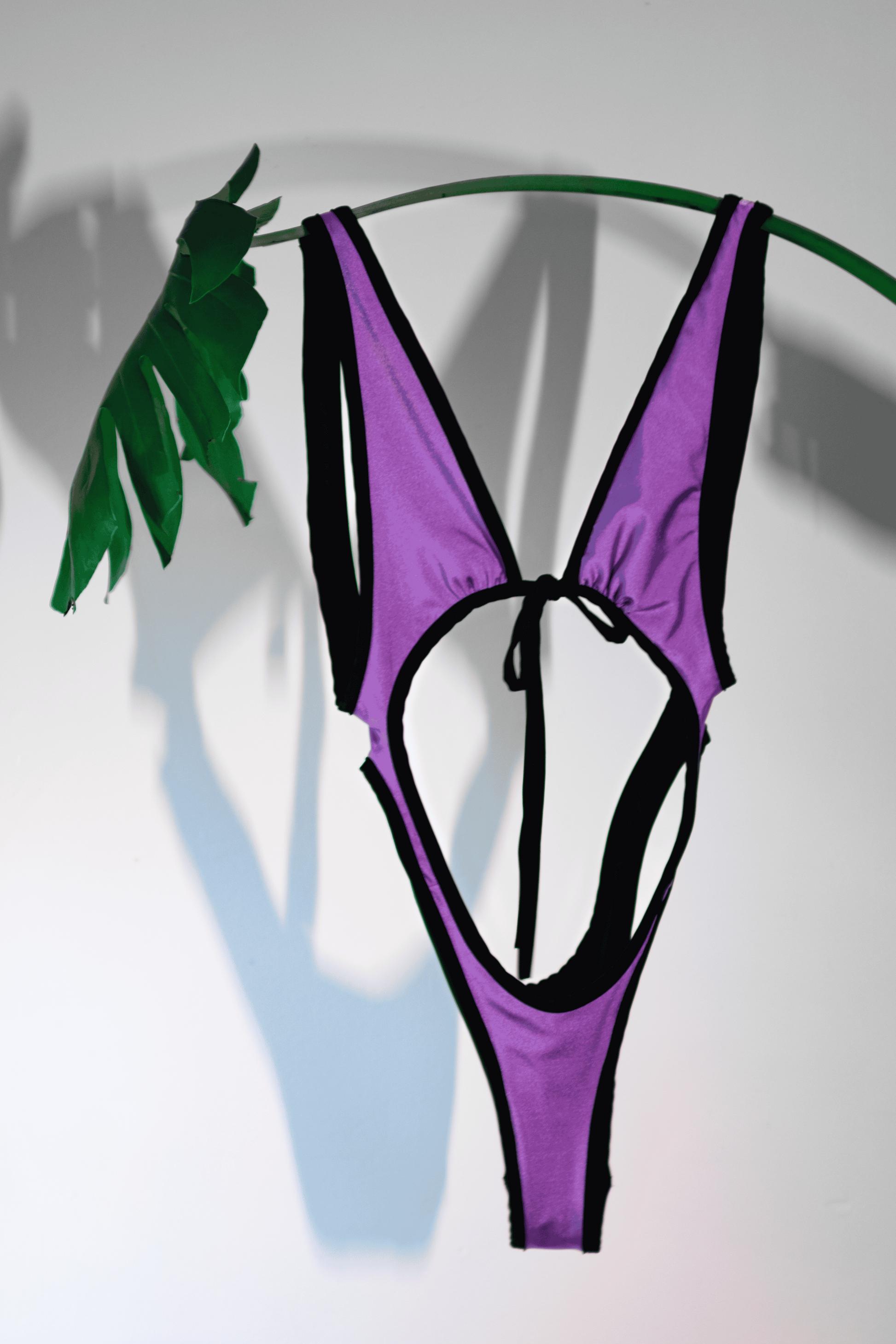 Purple and black bikini top on a white background with a plant shadow.