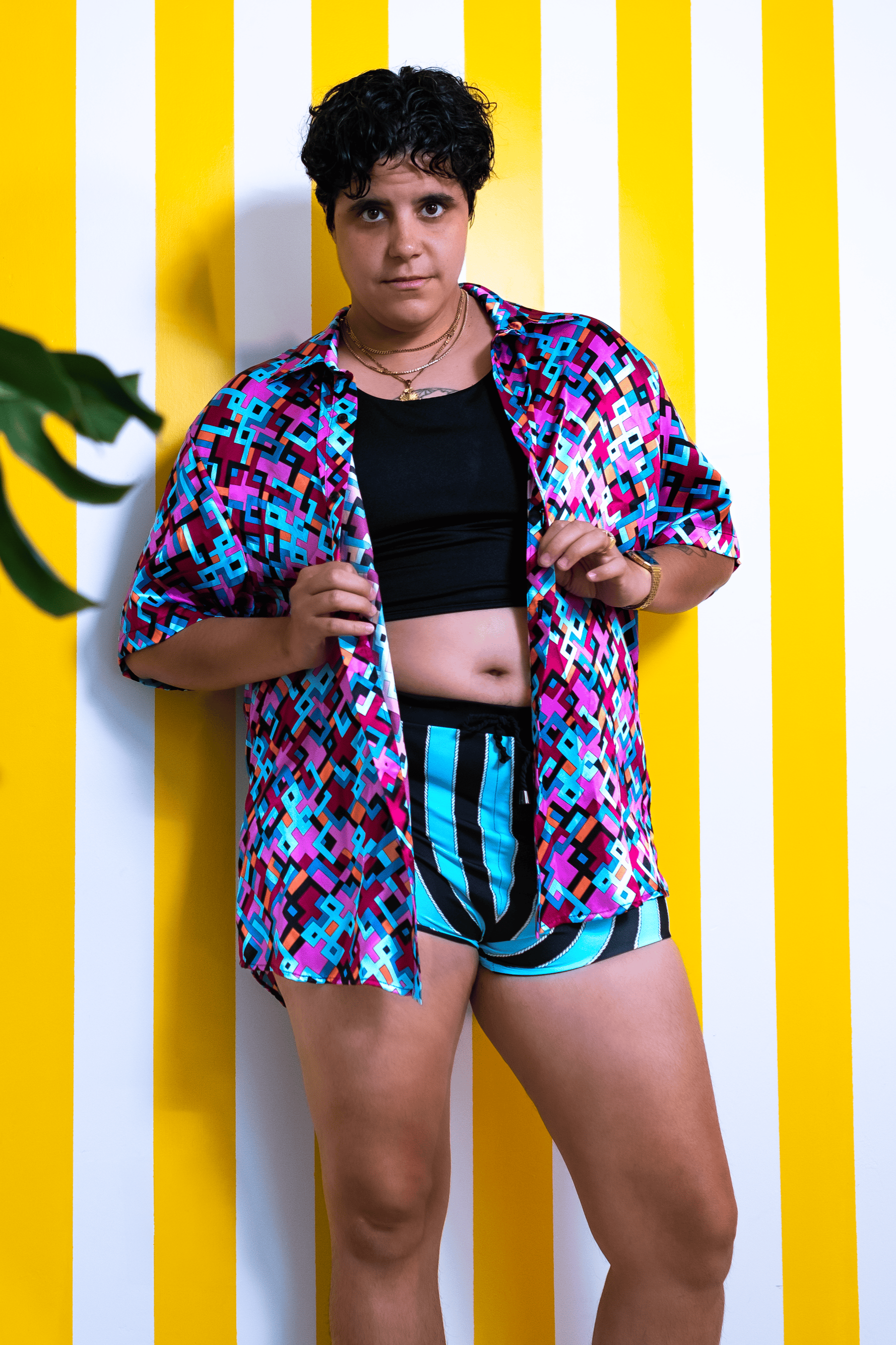 Person wearing a colorful shirt and black shorts against a yellow and white striped wall.