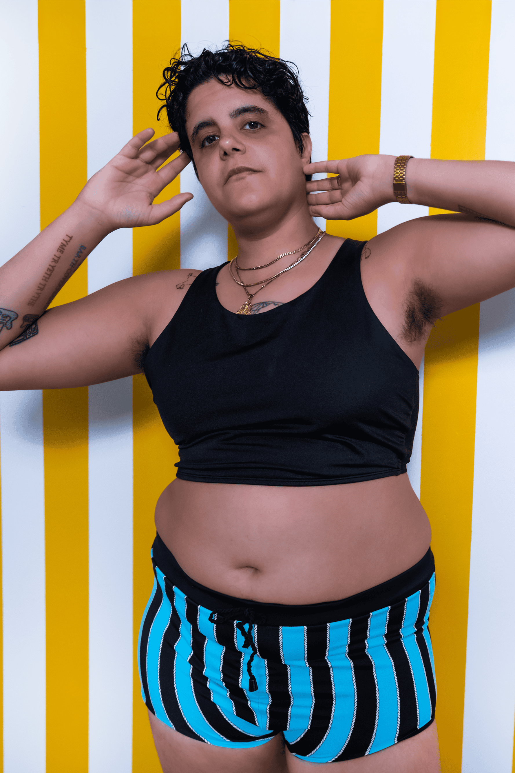 Person wearing a black tank top and blue striped shorts against a yellow and white striped background